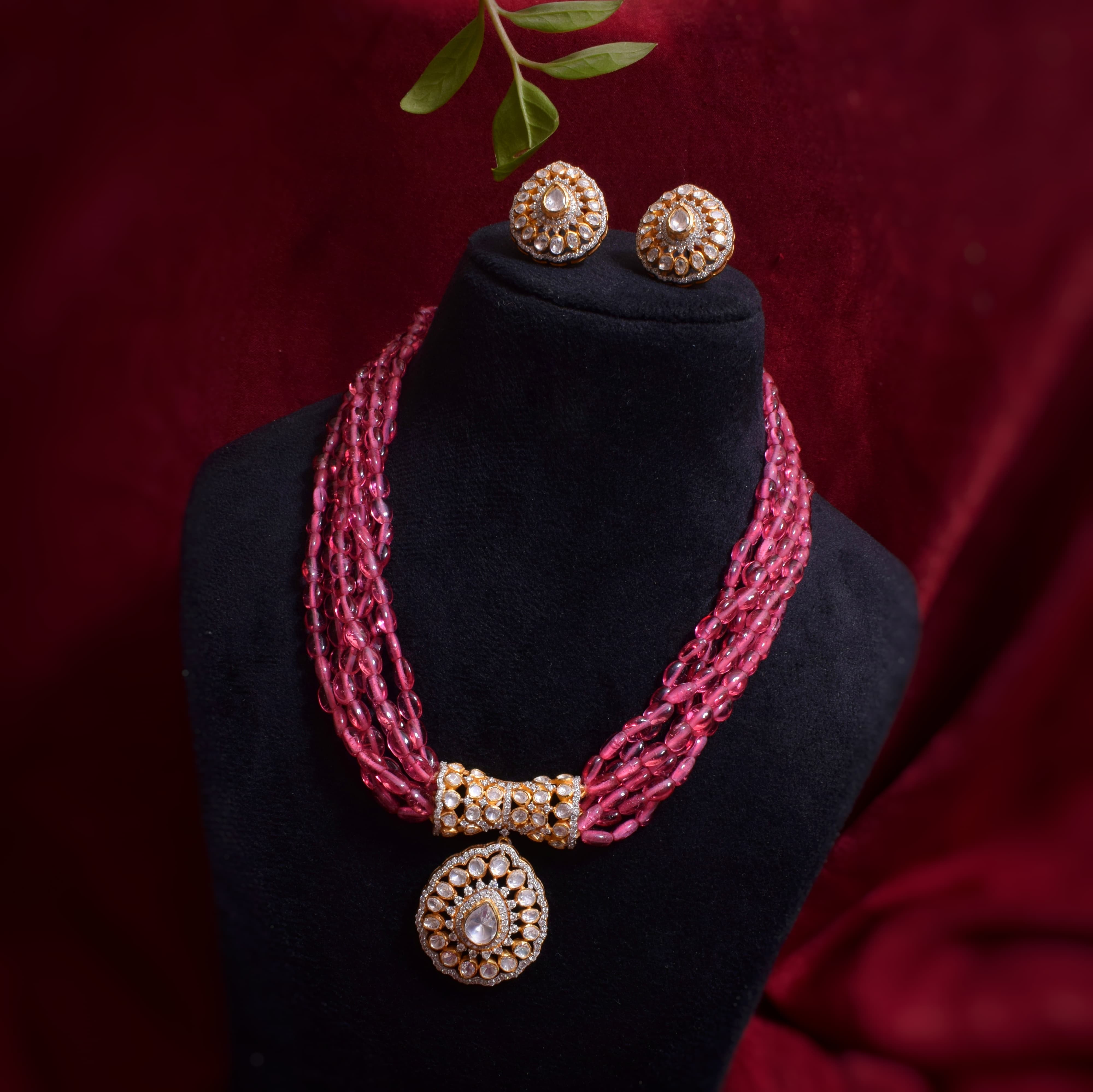 Pink necklace with gold accents on a black stand against a red background